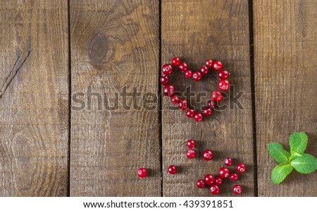 Cranberries in the form of heart with  mint on a wooden background
