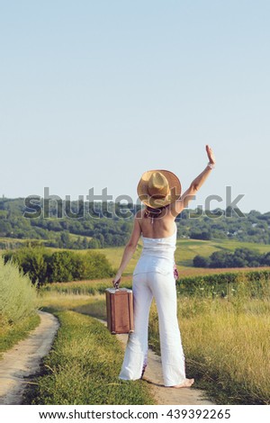 Backview of female holding retro suitcase, sunny outdoors country road background.