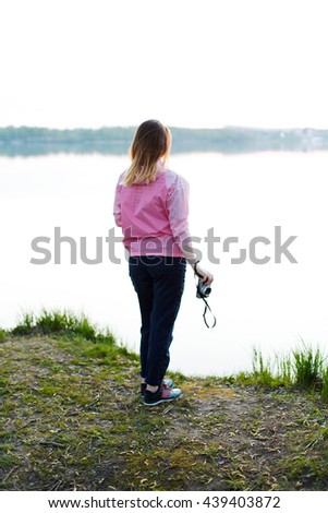 Young girl enjoying the peace and quiet near the lake at sunset. Female photographer with film camera