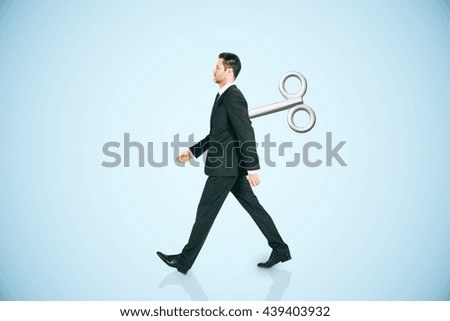Walking businessman with a wind-up key on his back walking on blue background. Concept of control