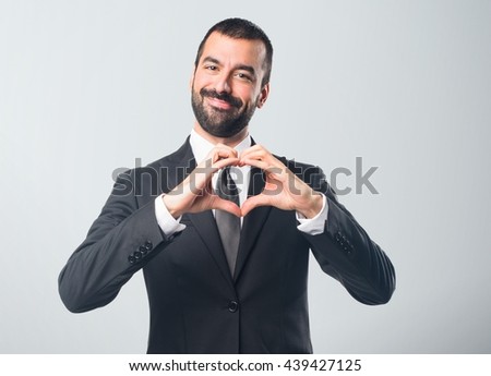 Businessman making a heart with his hands over grey background