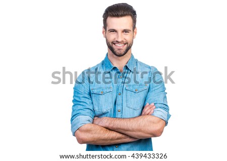 Casually handsome. Confident young handsome man in jeans shirt keeping arms crossed and smiling while standing against white background  Royalty-Free Stock Photo #439433326
