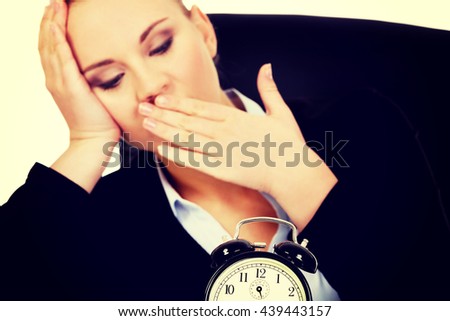 Tired business woman behind the desk with alarm clock
