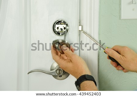 Closeup of a professional locksmith installing or repairing a new deadbolt lock on a house exterior door with the inside internal parts of the lock visible. Royalty-Free Stock Photo #439452403