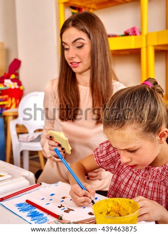 School girl with teacher woman painting on paper at table in primary painting school .