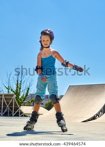 Girl wearing roller skates helmet riding on roller skates in skates park. Blue sky.