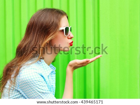 Woman in sunglasses sends an air kiss over colorful green background