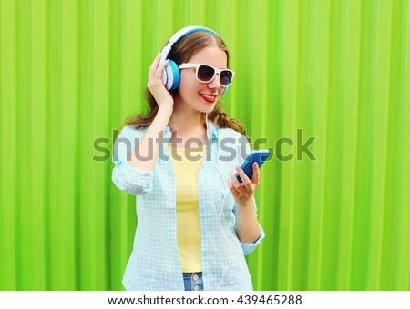 Pretty cool woman listens to music in headphones using smartphone over green background