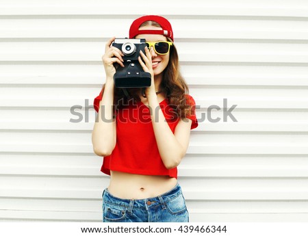Portrait of happy smiling young woman photographer taking picture on film camera wearing red baseball cap on white background