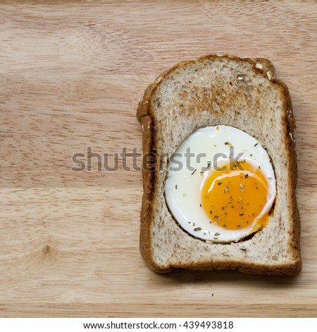 The close up square image of fried egg in bread on wooden texture