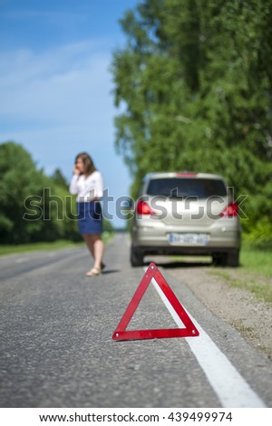 Female driver calling to assistance after breakdown. Broken car and red triangle warning sign. Selective focus