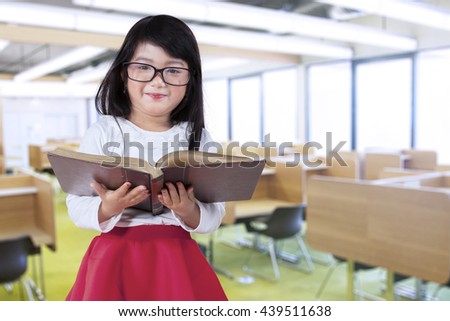 Portrait of a cute little girl wearing glasses and holding a book in the reading room