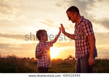 Father and son playing at the park at the sunset time. People having fun on the field. Concept of friendly family and of summer vacation.