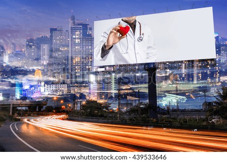 doctor holding red heart shape on blank billboard for advertisement at twilight time with light trails on the road at dusk, double exposure with city night.