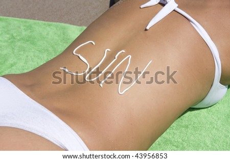 woman in white bikini lying on tropical beach with word sun written in sunlotion on back, guanacaste, costa rica, central america