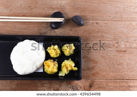 Buns of Pork stuffed and dumplings on a ceramic black plate. Bamboo chopsticks placed on a black stone.