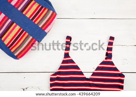 Travel concept - summer women's fashion with colorful striped bag and swimsuit on white wooden desk