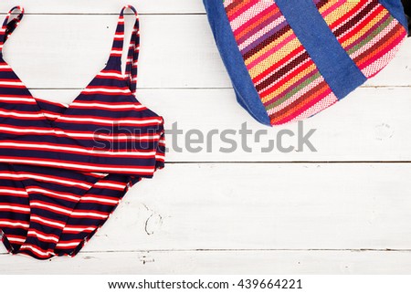 Travel concept - summer women's fashion with colorful striped bag and swimsuit on white wooden desk