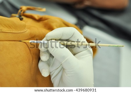 Leather bag coloring in leather factory, close view. A leather factory worker colouring a yellow leather bag at the finishing line.  Royalty-Free Stock Photo #439680931