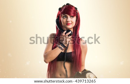 Young redhead girl talking to vintage phone over ocher background
