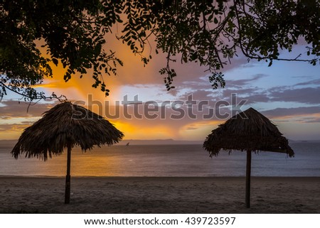 Beautiful ocean sunset landscape with orange lights and natural palm tree shed umbrellas. Indian Ocean, Madagascar, Ramena