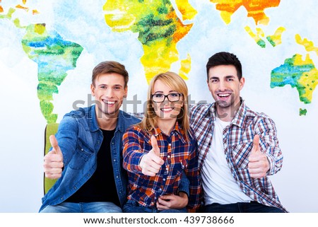 Life is good. Three model sit on sofa and show thumbs up in front of wall 
painted like a map of the world.
