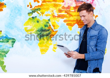 Lets check it. Handsome man look at tablet in front of wall painted like map of the world.