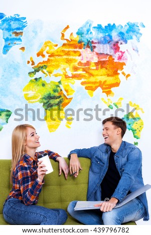 Sharing their ideas. Smiling young  woman holding a cup of coffee while man sitting near her in the rest area of the office.