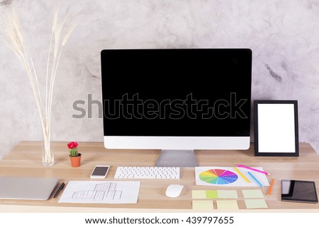 Creative designer desktop with blank computer monitor, white picture frame, keyboard, laptop, wheat spikes in vase and many other items. Mock up