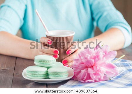 Woman hold paper cup of coffee and macaroons on table
