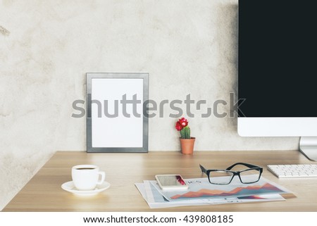 Creative desktop with computer monitor, business report, coffee cup, glasses and blank picture frame. Mock up