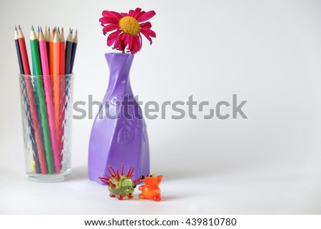 colorful pencils in glass cup near vase with flower and glass hedgehog and fox on white background 