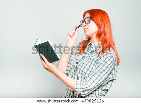 portrait of a girl thinking a notebook, red hair wearing glasses, isolated on a gray background