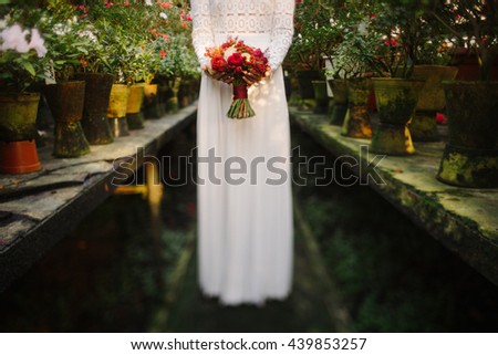 Intentionally blurred image of a bride in white simple dress hold a bouquet of red flowers in her hands. Tilt-shift lens used, soft selective focus.