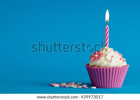 pink birthday cupcake with flowers and burning candle on blue background