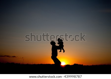 father and little child silhouettes play at sunset sky
