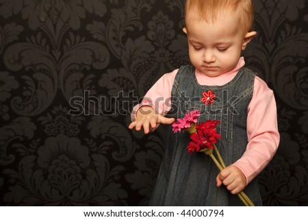 Portrait of a little girl with flowers on a background wall with patterned wallpaper.