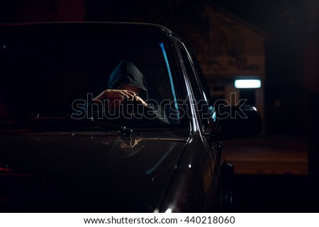 Night portrait of young sad driver girl with a hood in the black car.