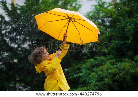 Chappie with a bright yellow umbrella in the warm summer rain. He loves a rain and rejoices. Large rain drops fall on an umbrella dome. Behind the back of the boy a beautiful greens of park. Royalty-Free Stock Photo #440274796