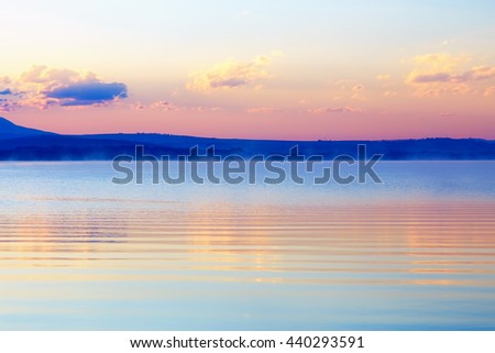 beautiful landscape with mountains and lake at dawn in golden, blue and purple tones