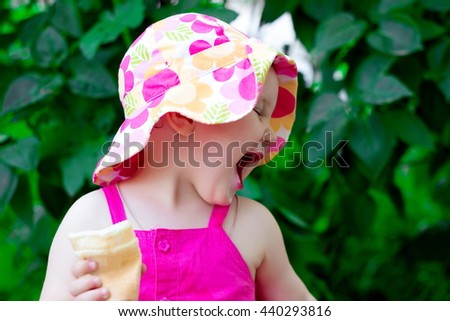 Little girl in the forest. The little girl walks in the summer. Beautiful girl in colored panama hat and bright colorful sundress with ice cream in the hands of eating, sitting on a tree stump.