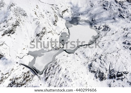 aerial shot, from a small plane, of Gemelli lakes covered with melting ice and snow , shot on a very bright springtime day with recent snow in Orobie mountains, Bergamo , Italy

