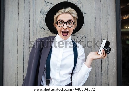 Happy surprised young woman photographer in black hat holding photo camera