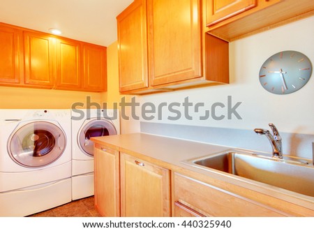 Laundry room with modern appliances and light tone wooden cabinets.