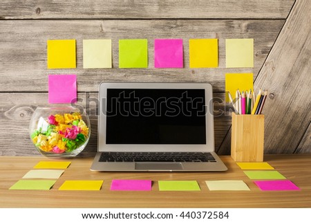 Creative vibrant desktop with blanklaptop screen, colorful stickers, pencils and decorative glass bowl with crumpled paper. Mock up
