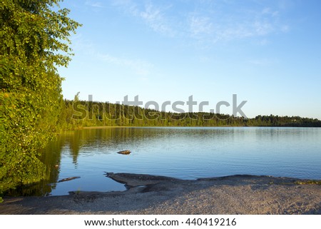 Beautiful evening by the lake during sunset. Some rocks are in the water. Birch leaves are glowing due to sun going down. Image taken in Finland.