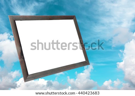 Old wood photo frame with white copy space inside on the background of the blue sky with fluffy white clouds. Blank space for any text (advertising, announcement). Toned colors 
