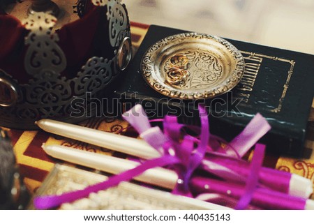 Wedding rings lie on a golden plate behind crown and candles on the table in church