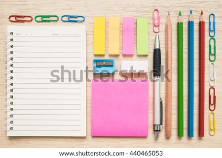 Top view flat lay of colorful set of stationery tool and equipment - notepad, paper clips, sticky notes, pen, pencil, colored pencils, eraser, sharpener - on wooden background - back to school