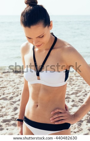 The slender brunette in black and white bikini on the beach, her tanned body of water drops. Morning summer vacation on the coast.